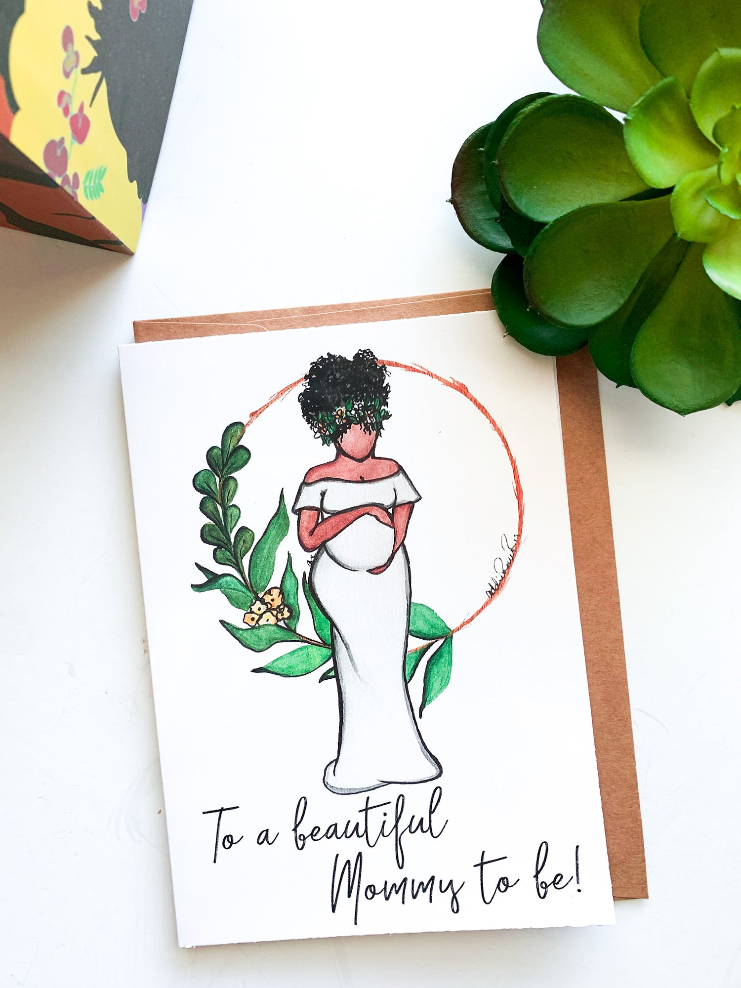 Hand drawn water color card of a pregnant African American woman gently cradling her belly. Her hair has green leaves and baby breath flowers in it, she is wearing an off the shoulder white dress, there is a a circle behind her with green foliage on one side of the circle. The Text says, To a Beautiful Mommy to Be by artist Addie Rawr