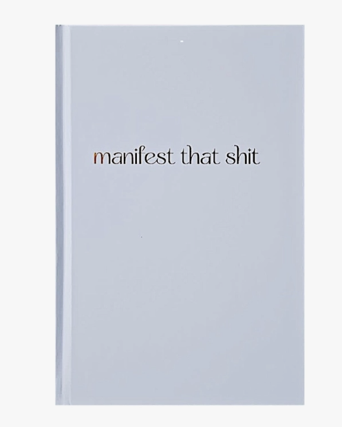 White hardbound journal with the words manifest that shit in gold foil