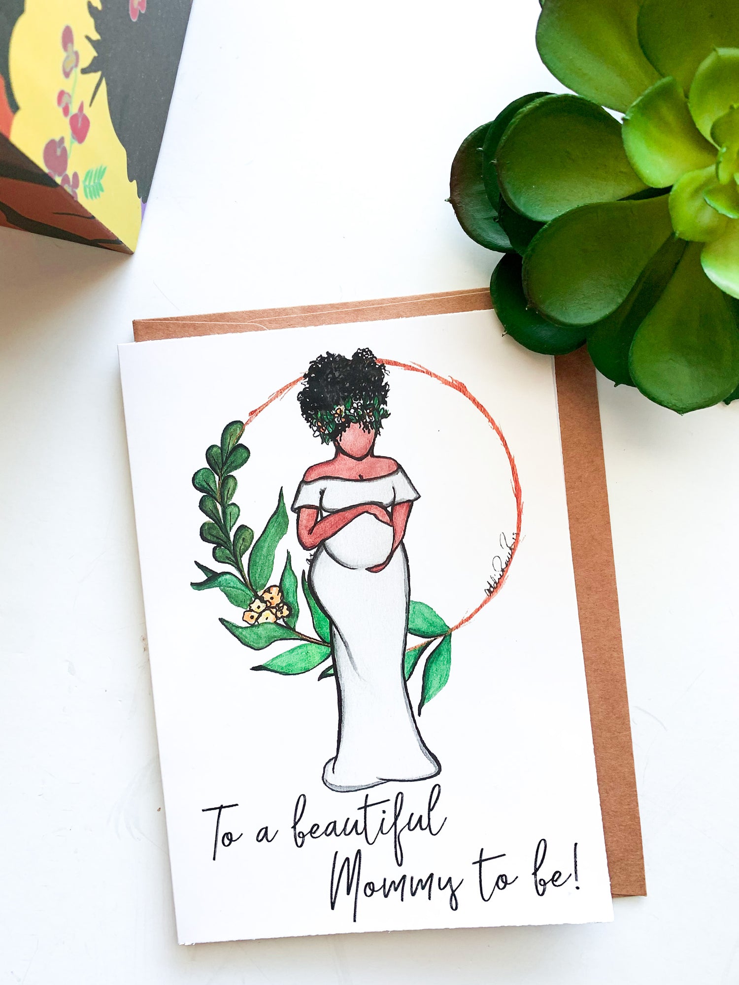 Hand drawn water color card of a pregnant African American woman gently cradling her belly. Her hair has green leaves and baby breath flowers in it, she is wearing an off the shoulder white dress,  there is a a circle behind her with green foliage on one side of the circle. The Text says, To a Beautiful Mommy to Be by artist Addie Rawr