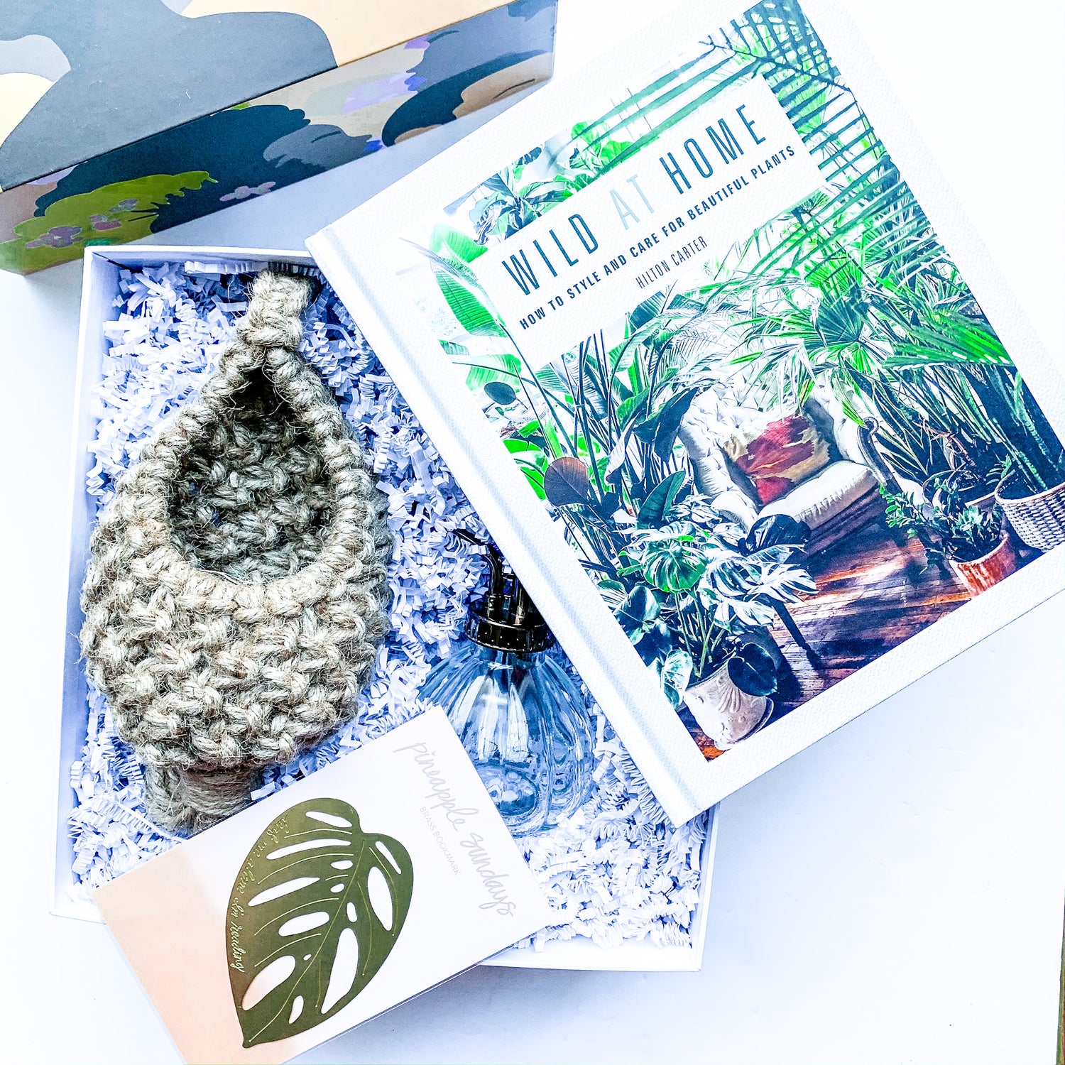 Gift box featuring a jute plant pod, for a small plant, a clear plant mister, a brass monstera bookmark, a book on how to style and care for your beautiful plants by Hilton Carter